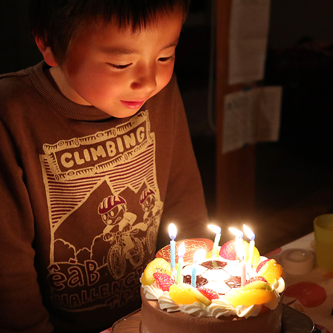 バースデーケーキのろうそくの火を笑顔で見つめる男の子